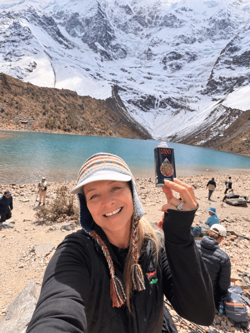 Hiker holds tea can beside turquoise alpine lake